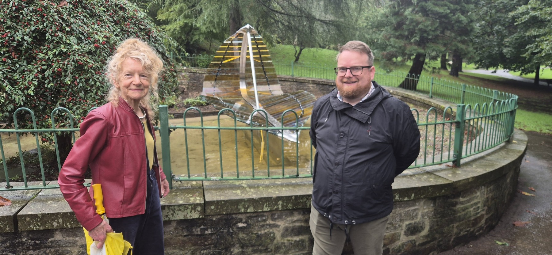 Artist Amber Hiscott and Cllr Elliott King standing either side of the Leaf Boat sculpture at Cwmdonkin Park