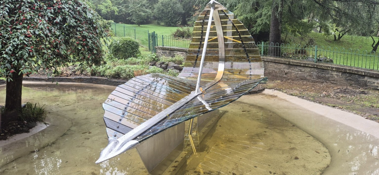 The steel and glass Leaf Boat sculpture standing in the refilled ornamental pond at Cwmdonkin Park, Swansea