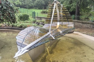 The steel and glass Leaf Boat sculpture standing in the refilled ornamental pond at Cwmdonkin Park, Swansea