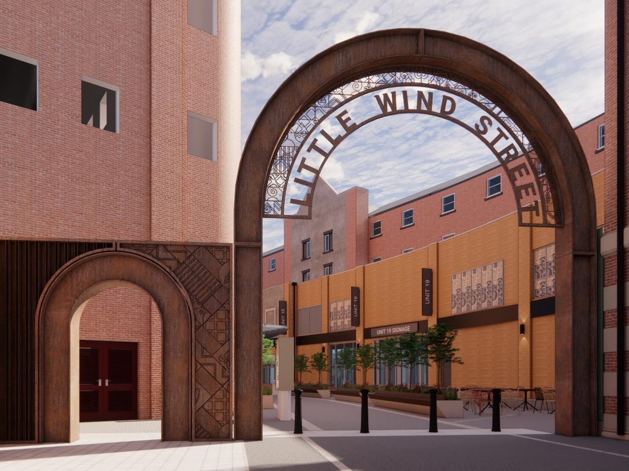Architect's render of a tall rust-coloured steel arch reading Little Wind Street across the entrance to a brick-lined lane, with a smaller matching arch beside it and planters and cafe tables beyond