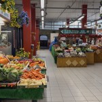 Fruit and vegetables displayed on the WD Seward and Sons stall inside Llanelli's indoor market, with produce stalls and a shopper along the aisle