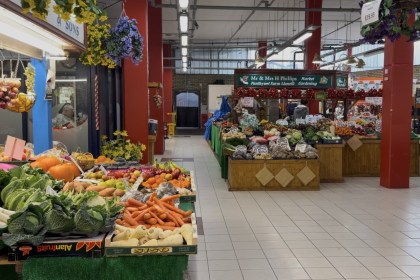Fruit and vegetables displayed on the WD Seward and Sons stall inside Llanelli's indoor market, with produce stalls and a shopper along the aisle