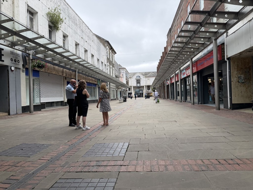 Pedestrianised Vaughan Street in Llanelli with glass canopies over the shops, the former Tinhouse pub on the left and Home Bargains on the right, looking towards the clock arch
