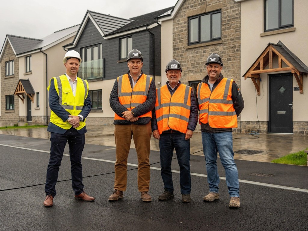 Four men in hi-vis vests and hard hats standing in a new street of stone-fronted houses at Maes y Teirw, Carmarthen