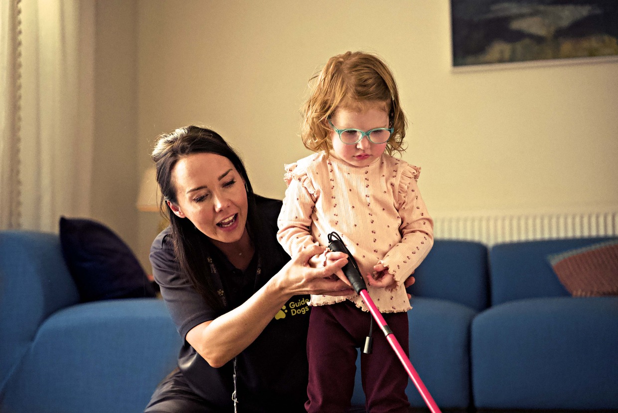 A Guide Dogs habilitation specialist kneeling beside Martha Thompson and guiding her hands on a pink cane