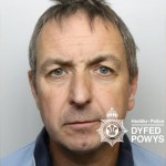 Custody image of Michael Fox, a middle-aged man with grey hair in a light blue polo shirt, with the Dyfed-Powys Police watermark