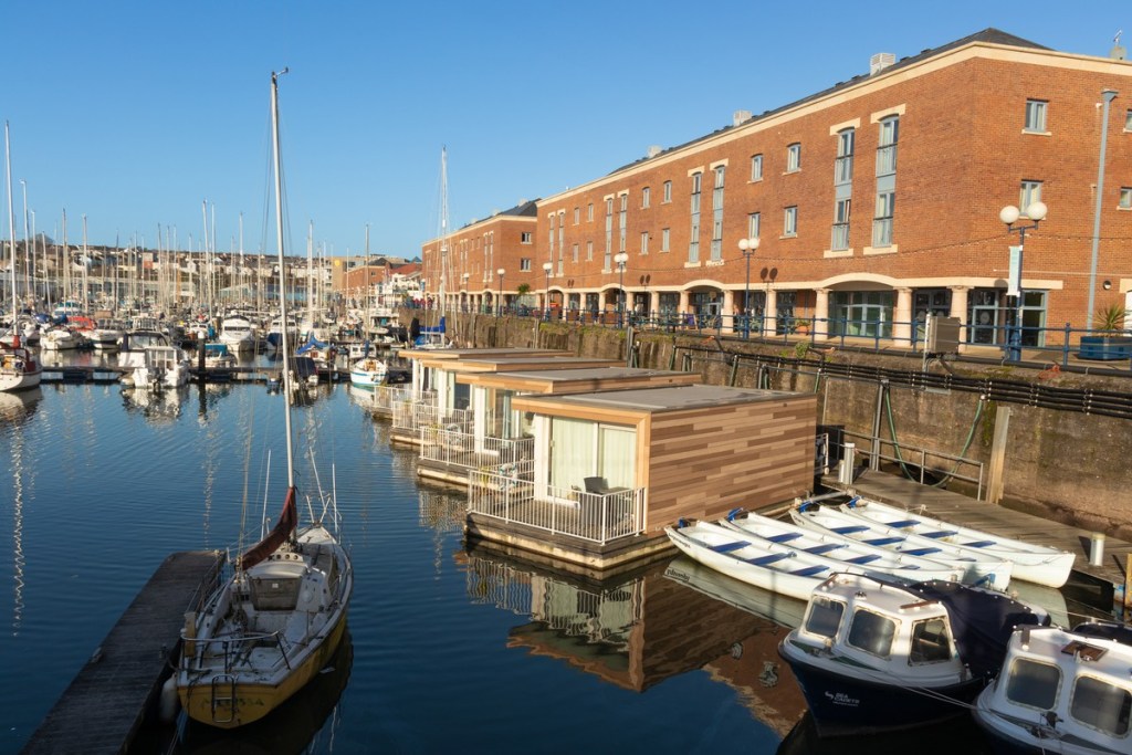 Milford Haven marina with yachts moored along pontoons, floating waterside pods and the red brick waterfront buildings behind