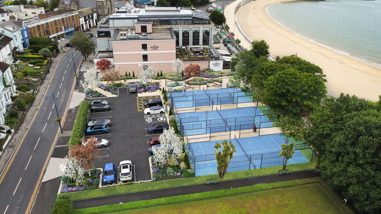 Aerial artist's impression of three blue padel courts and a landscaped car park on the former tennis courts beside the Oyster House, with Mumbles beach and the bay beyond