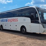 A white National Express coach parked on dry ground at the Glastonbury Festival coach station under a blue sky