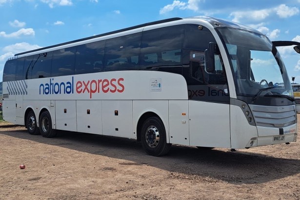 A white National Express coach parked on dry ground at the Glastonbury Festival coach station under a blue sky