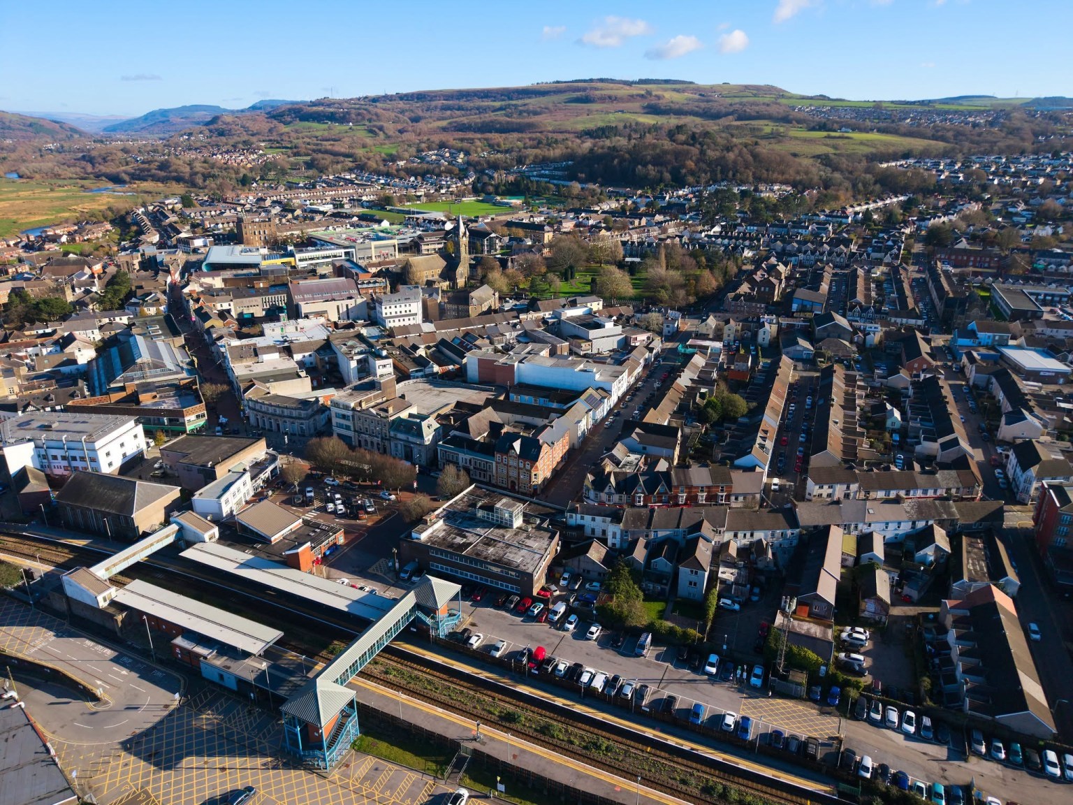 Aerial view of Neath town centre with the railway station and car parks in the foreground and hills behind