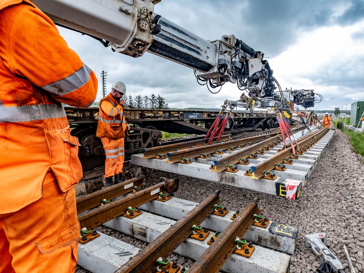 Railway engineers in orange hi-vis clothing watch as a crane lowers a new section of track with concrete sleepers into place