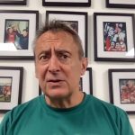 Scarlets director of rugby Nigel Davies in a green club polo shirt speaking at a press conference in front of a wall of framed rugby photographs