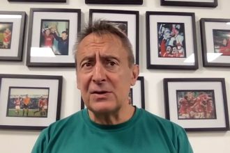 Scarlets director of rugby Nigel Davies in a green club polo shirt speaking at a press conference in front of a wall of framed rugby photographs