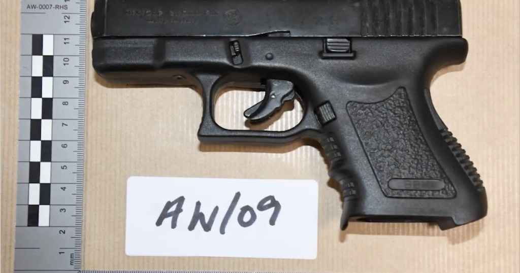 Evidence photograph of a black BB-type handgun beside forensic rulers and an exhibit label