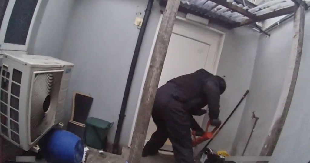 Bodycam footage of police officers forcing entry through a rear gate during a raid