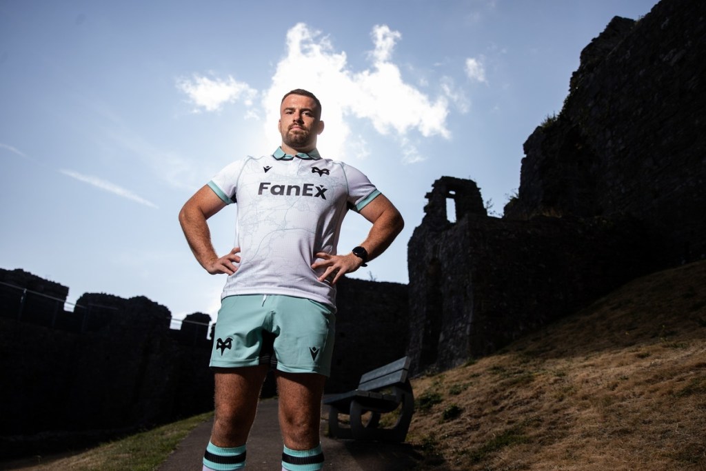 An Ospreys player in the white 2026/27 away shirt with a teal street map pattern, standing at a ruined castle