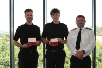 PC Taylor Rees and PC Guto Dafydd holding their bronze bravery medals in presentation boxes, with Chief Constable Ifan Charles in uniform