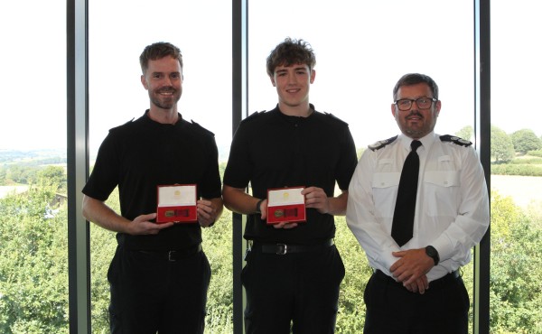 PC Taylor Rees and PC Guto Dafydd holding their bronze bravery medals in presentation boxes, with Chief Constable Ifan Charles in uniform