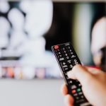 A person holding a black TV remote control in front of a television