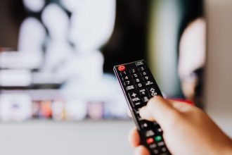 A person holding a black TV remote control in front of a television