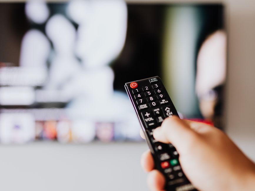 A person holding a black TV remote control in front of a television