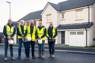 Five men in hi-vis vests holding hard hats in front of new detached houses at Priory Fields, St Clears