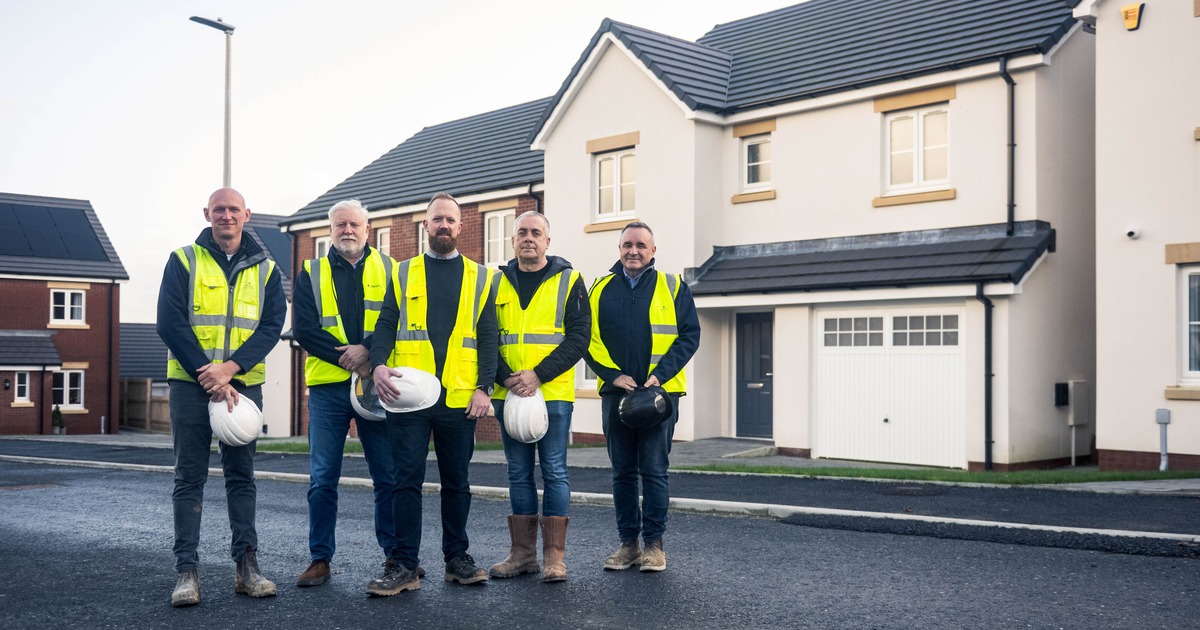 Five men in hi-vis vests holding hard hats in front of new detached houses at Priory Fields, St Clears