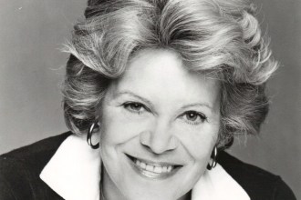 Black and white studio portrait of actress Rachel Roberts smiling, with swept-back fair hair, hoop earrings and a white collar over a dark cardigan