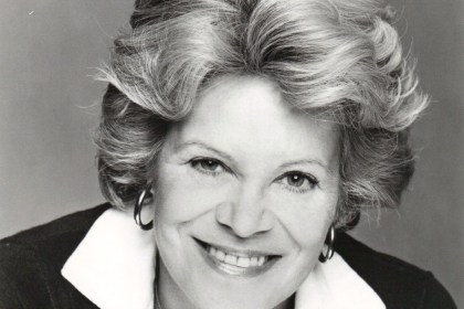 Black and white studio portrait of actress Rachel Roberts smiling, with swept-back fair hair, hoop earrings and a white collar over a dark cardigan