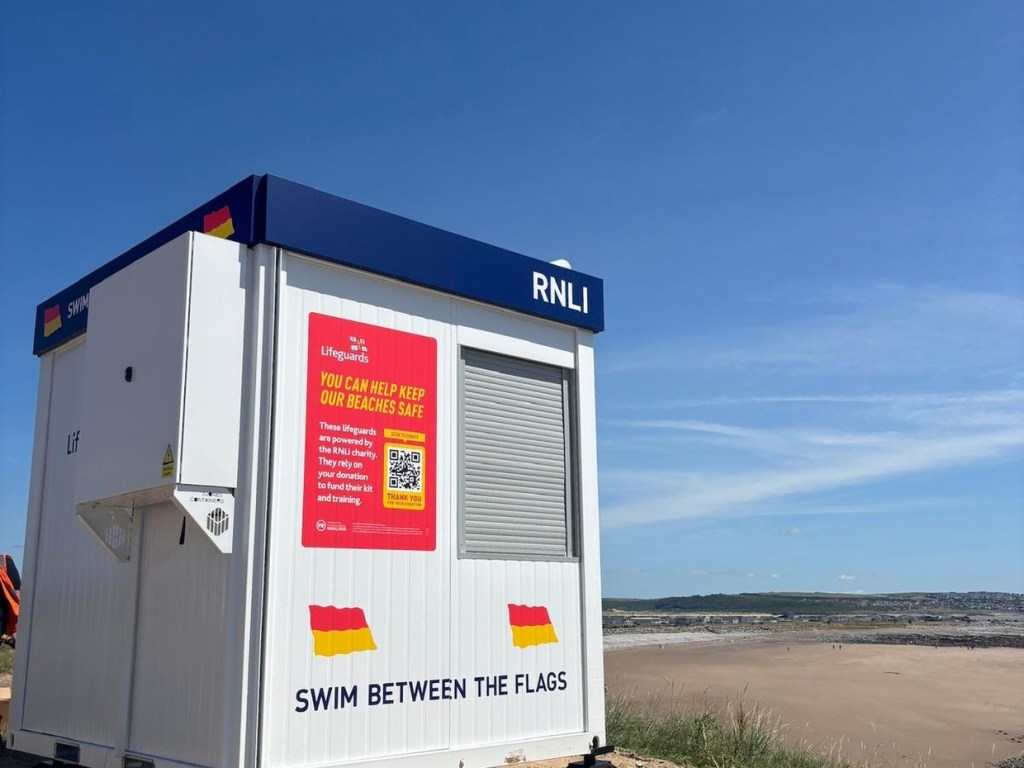 The front of a new RNLI beach lifeguard unit with swim between the flags signage and a donation poster