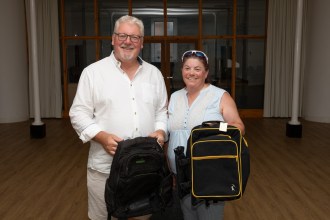 Peter Lynn and Paula Stockley standing in a hall each holding a black rucksack