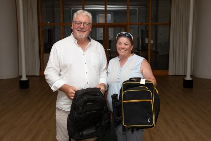 Peter Lynn and Paula Stockley standing in a hall each holding a black rucksack
