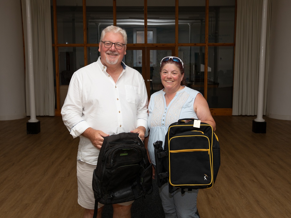 Peter Lynn and Paula Stockley standing in a hall each holding a black rucksack