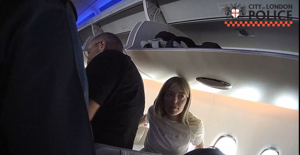 Still from City of London Police footage showing Sally Harris looking up towards the camera in an aircraft cabin during her arrest