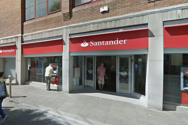 The red Santander fascia and glass entrance of the bank's branch on Union Street, Swansea, with customers at the door and a cash machine