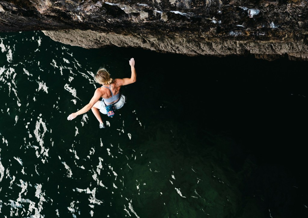 Overhead view of Shauna Coxsey on the cliff edge with dark green water filling the frame below her