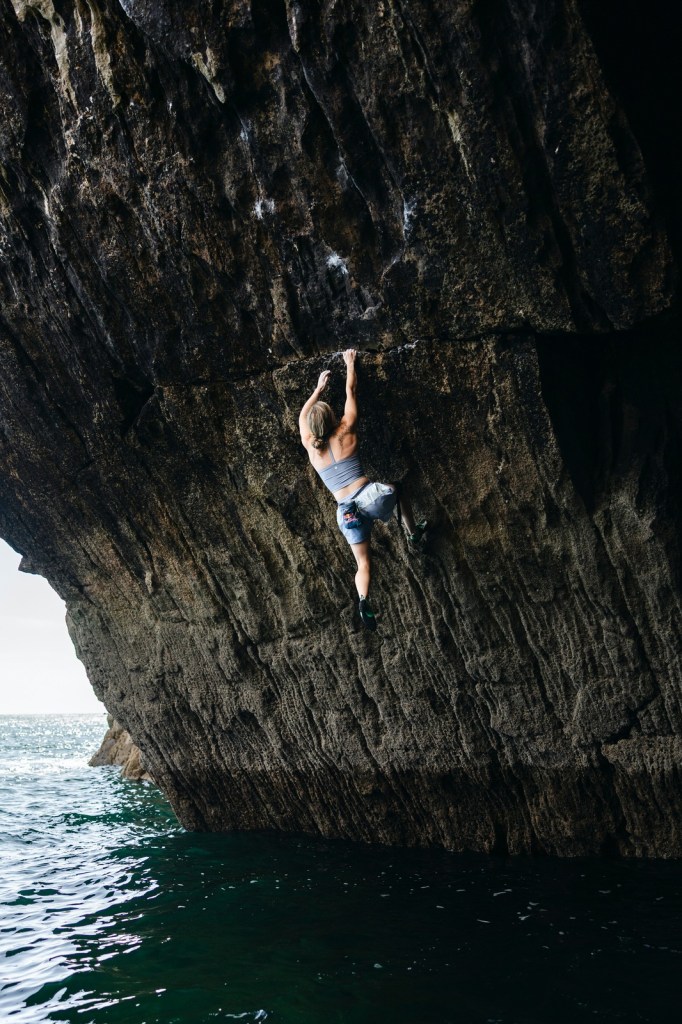 Shauna Coxsey climbing the full height of the sea cliff at Skrinkle Haven with the water directly below