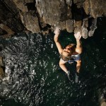 Shauna Coxsey hanging beneath the overhanging roof of The Olympiad at Skrinkle Haven, seen from above with the sea below her