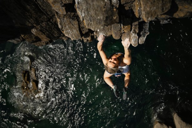 Shauna Coxsey hanging beneath the overhanging roof of The Olympiad at Skrinkle Haven, seen from above with the sea below her