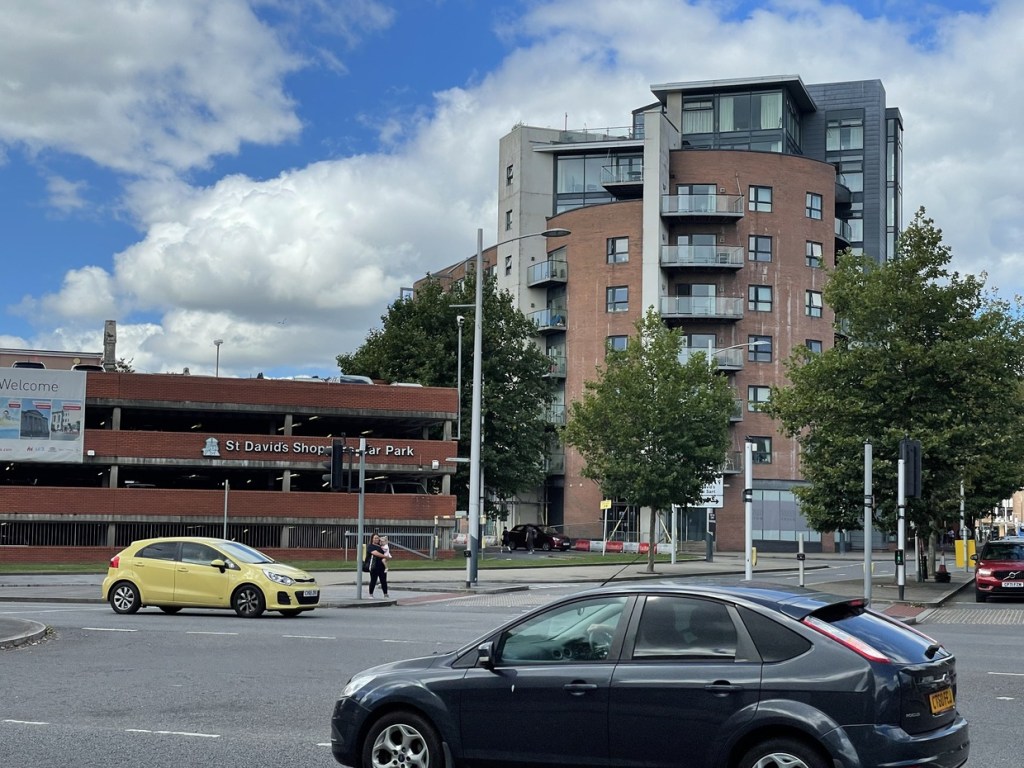 The red-brick St David's Shoppers Car Park seen across Oystermouth Road traffic, with a tower of flats behind