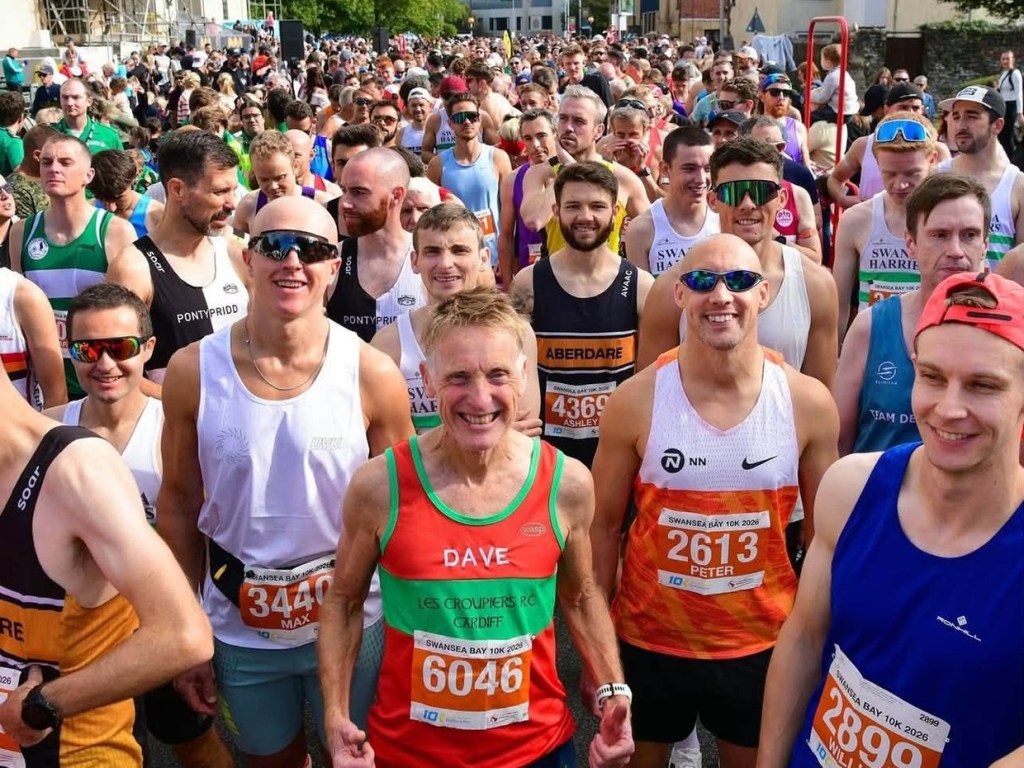 Hundreds of runners in club vests and race bibs packed on the start line, smiling, with scaffolding on the Guildhall behind