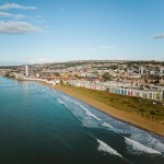 Aerial view of Swansea Bay beach with waves breaking on the sand, seafront apartments and Meridian Tower behind