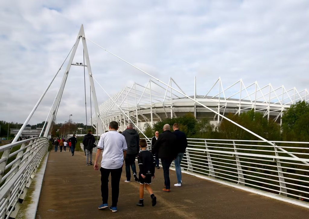 Supporters, including a boy in a Swansea City shirt, walking across the white cable-stayed footbridge towards the Swansea.com Stadium