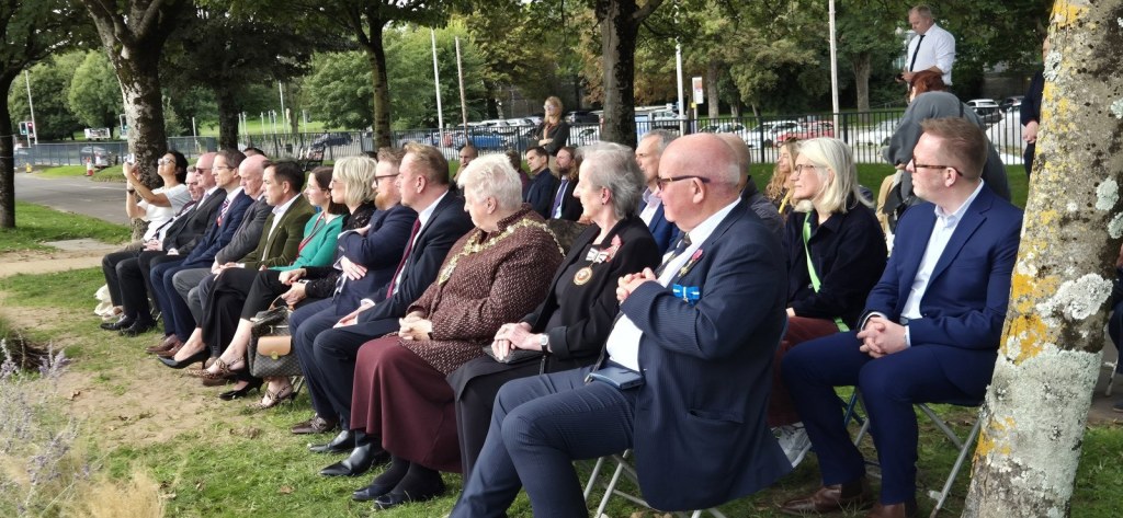 Rows of seated guests on the grass beside the promenade, including the Lord Mayor wearing her chain of office