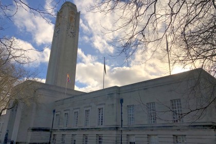 Swansea Guildhall's clock tower and stone frontage under a bright cloudy sky, with bare winter branches overhead and a Pride flag flying