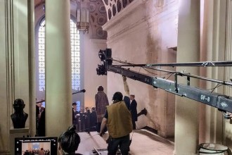 Film crew operating a camera crane on tracks inside the Guildhall's grand corridor in Swansea, with costumed actors beneath the honeycomb ceiling