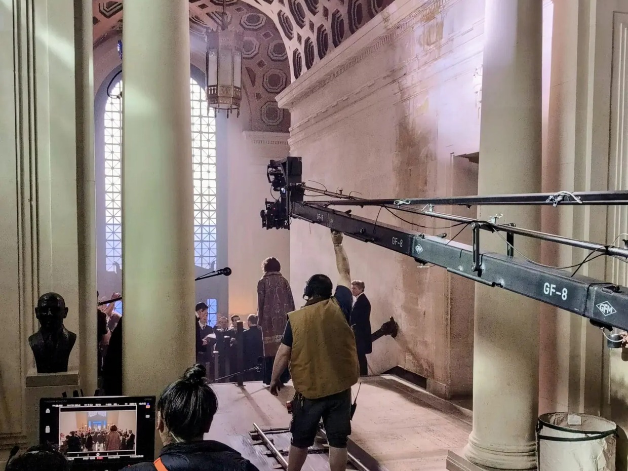 Film crew operating a camera crane on tracks inside the Guildhall's grand corridor in Swansea, with costumed actors beneath the honeycomb ceiling