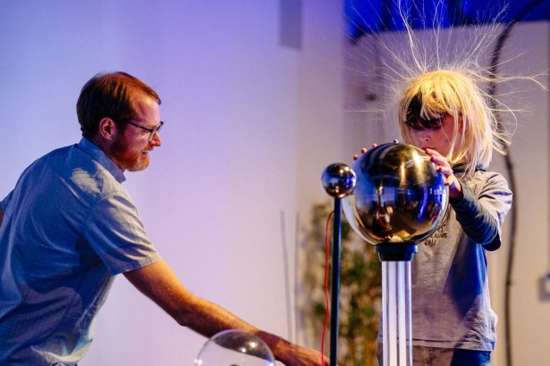 A child's hair stands on end as they touch a Van de Graaff generator at the Swansea Science Festival, watched by a smiling demonstrator