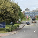 The entrance road to Swansea University's Singleton Park campus, with the blue bilingual university sign on the left and the main building at the end of the drive